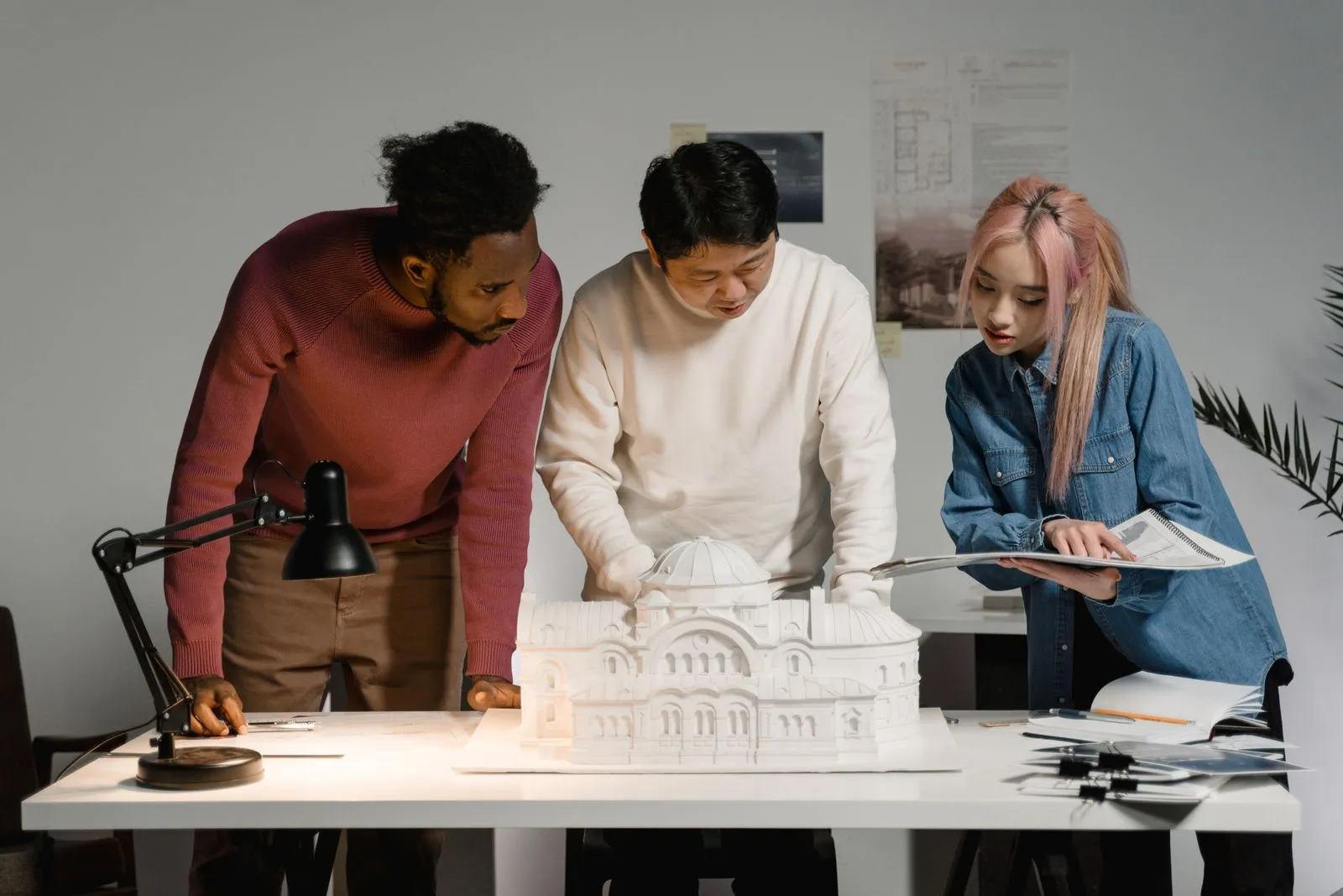 Three architects studying a white scale model of a building on a studio table
